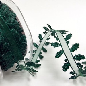 May include: A spool of dark green ribbon featuring a die-cut holly leaf and berry pattern along both edges. The ribbon is made of a sheer, translucent material with a solid center strip and intricate, jagged leaf shapes extending outward.
