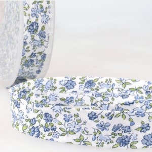 May include: A roll of white cotton ribbon with a blue and green floral print. The ribbon is approximately 2.5 cm wide.