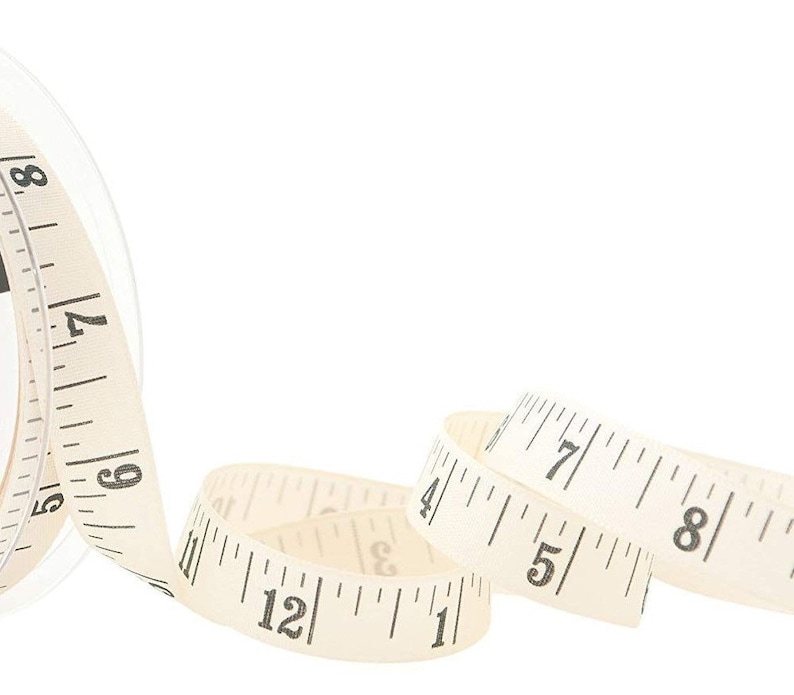 May include: A white fabric measuring tape with black numbers, rolled up and partially unrolled. The tape measures in inches.