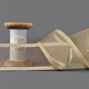 May include: Gold mesh ribbon with a gold metallic edge. The ribbon is wound around a spool with the label "Plum Pretty".
