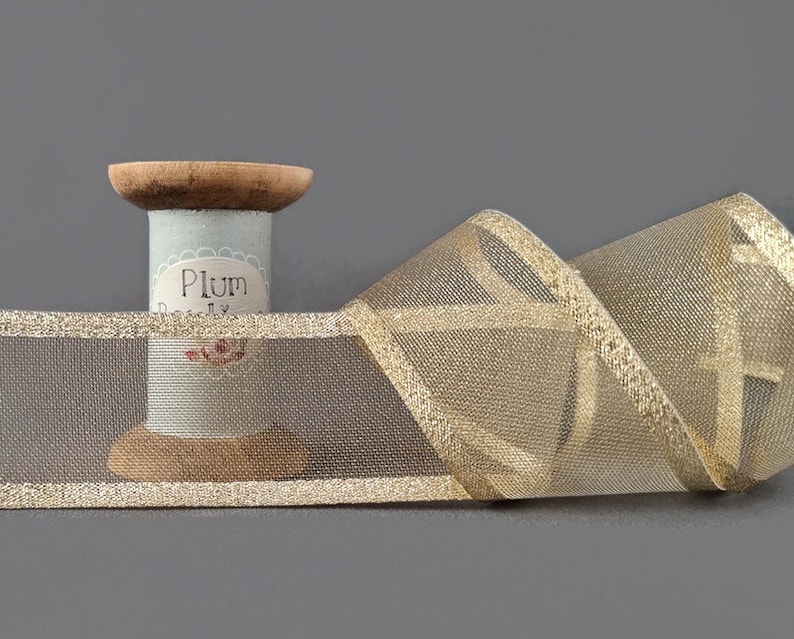 May include: Gold mesh ribbon with a gold metallic edge. The ribbon is wound around a spool with the label "Plum Pretty".