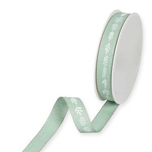 Puede incluir: Un rollo de cinta verde claro con un patrón floral blanco. La cinta está en un carrete blanco.