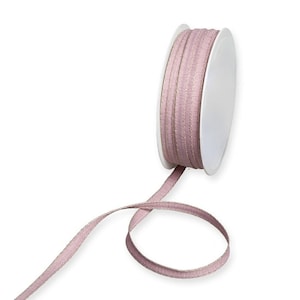 May include: A spool of pink and beige ribbon with a white label. The ribbon is woven and has a subtle texture.