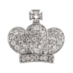 Pode incluir: Um amuleto de coroa de prata com strass transparentes. A coroa tem um topo pontudo e uma base arredondada.