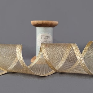 May include: Gold metallic ribbon with a sheer mesh texture. The ribbon is wound around a spool labeled "Plum Boutique".