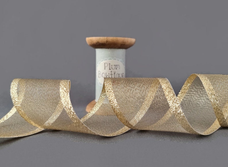 May include: Gold metallic ribbon with a sheer mesh texture. The ribbon is wound around a spool labeled "Plum Boutique".