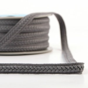 May include: Grey braided trim with a subtle herringbone pattern. The trim is shown wound on a spool.