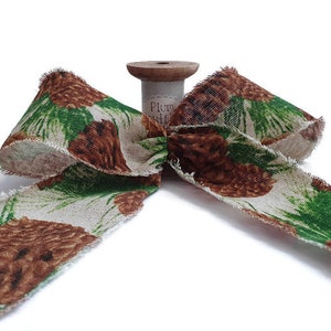 May include: A brown and green fabric ribbon with a pine cone pattern. The ribbon is tied into a bow and is on a spool.