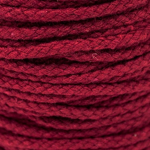 May include: Close-up of a reel of thick, red cotton cord. The cord is tightly wound and has a slightly textured surface.