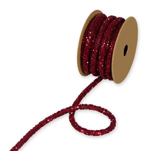 Könnte beinhalten: Eine Spule rotes Glitzerband. Das Band hat eine tief burgunderrote Farbe und ist mit glitzernden Glitzer bedeckt. Die Spule besteht aus Pappe und hat eine neutrale, beige Farbe. Das Band ist abgewickelt und gewellt.