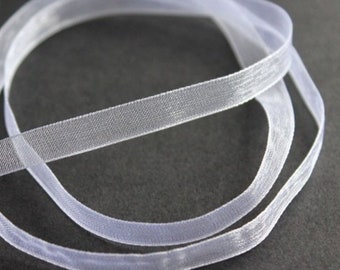 May include: White sheer ribbon with a subtle shimmer. The ribbon is rolled up and the edges are slightly curled.