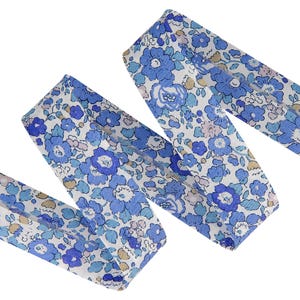 May include: A length of fabric ribbon featuring a repeating floral pattern in shades of blue, light blue, and white. The design consists of various small and medium-sized flower blossoms and leaves arranged across a white background.
