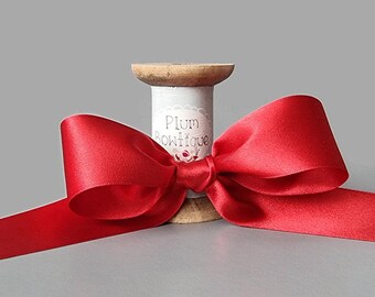 May include: A red satin ribbon tied into a bow on a wooden spool. The spool is labeled "Plum Boutique".