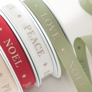 May include: Spools of decorative ribbon in cream, red, white, and sage green. Each ribbon features a repeating pattern of a star and a word: JOY, NOEL, PEACE, and LOVE. The ribbons are ideal for holiday crafts and gift wrapping.