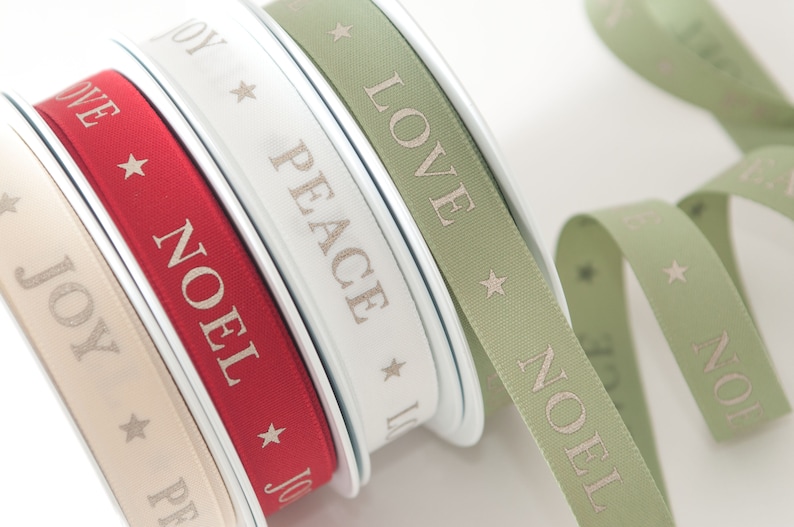May include: Spools of decorative ribbon in cream, red, white, and sage green. Each ribbon features a repeating pattern of a star and a word: JOY, NOEL, PEACE, and LOVE. The ribbons are ideal for holiday crafts and gift wrapping.