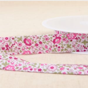 May include: A spool of white fabric ribbon with a pink floral print. The ribbon is approximately 1 inch wide.
