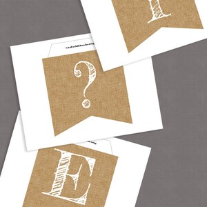 K&ouml;nnte beinhalten: Ein bedruckbarer Jutebanner mit den Buchstaben "E" und "?" in Wei&szlig;. Die Buchstaben sind in handschriftlicher Form und befinden sich auf einem braunen Jutehintergrund.