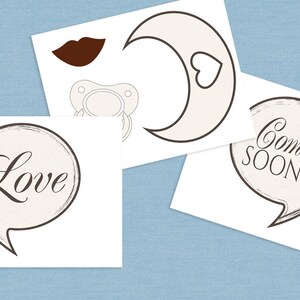 Pu&ograve; includere: Un set di accessori per foto booth per baby shower stampabili con un ciuccio, una luna crescente con un cuore, un fumetto con la parola "Love" e un fumetto con il testo "Coming Soon!"