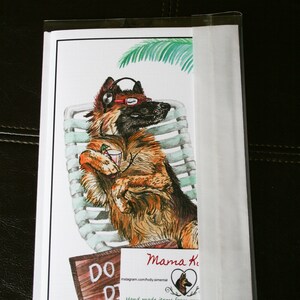 May include: A watercolor illustration of a German Shepherd dog wearing headphones and sunglasses, relaxing on a lounge chair under a palm tree. The dog is holding a drink in its paw. The illustration is on a white card with a brown wooden sign that says "DO DO" and a small business card with the text "Mama Ki" and the website address "www.mamakikis.e".