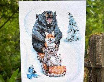 May include: A rectangular art print featuring a watercolour illustration of a black bear, a red fox, a raccoon, and a white rabbit riding a wooden sled down a snowy hill, with a blue jay flying nearby and a snow-covered evergreen tree in the background.