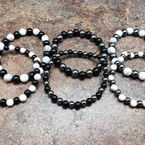 May include: Five bracelets made of black and white beads. The bracelets are stacked on top of each other.