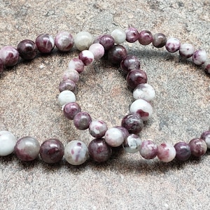 May include: Two bracelets made of pink and white gemstone beads. The bracelets are made of round beads and are stacked on top of each other.