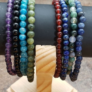 May include: A set of eight beaded bracelets in various colors, including purple, blue, green, and red. The bracelets are displayed on a wooden stand.