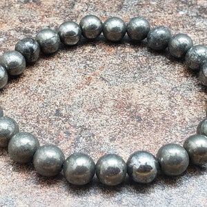 May include: A bracelet made of round, dark gray pyrite beads. The beads are smooth and have a slightly metallic sheen.