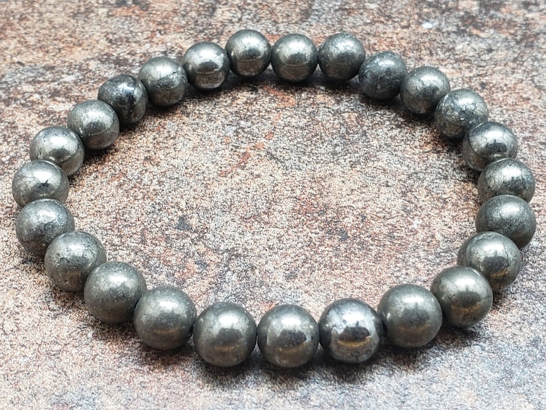 May include: A bracelet made of round, dark gray pyrite beads. The beads are smooth and have a slightly metallic sheen.