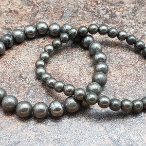 May include: Two silver beaded bracelets made of pyrite, a metallic mineral with a shimmering, iridescent finish.