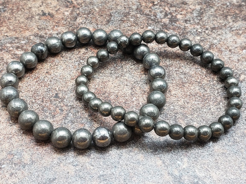 May include: Two silver beaded bracelets made of pyrite, a metallic mineral with a shimmering, iridescent finish.