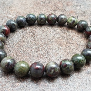 K&ouml;nnte beinhalten: Ein Armband aus gr&uuml;nen, schwarzen und roten Edelsteinen mit runden Perlen.