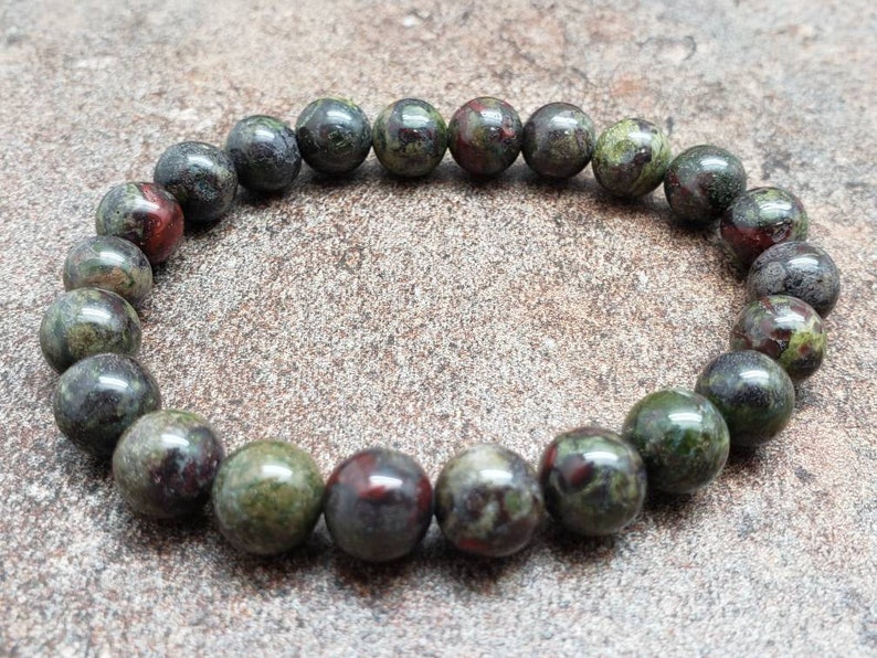 K&ouml;nnte beinhalten: Ein Armband aus gr&uuml;nen, schwarzen und roten Edelsteinen mit runden Perlen.
