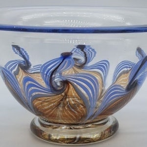 May include: A clear glass bowl with a blue rim and a swirling pattern of blue, brown, and gold. The bowl has a small foot.