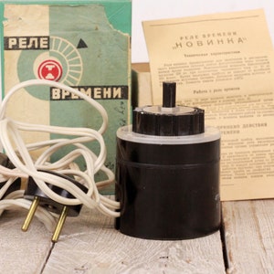 May include: A black time delay relay with a white cord and plug. The relay is labeled "Реле времени" and "Новинка".