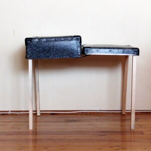 May include: A black and gray suitcase with wooden legs, used as a table. The suitcase is open and the top is folded down to create a flat surface.