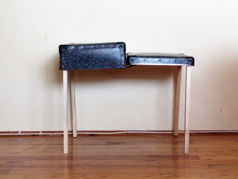May include: A black and gray suitcase with wooden legs, used as a table. The suitcase is open and the top is folded down to create a flat surface.