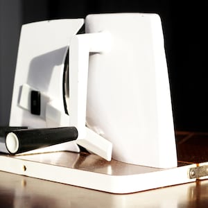 Pode incluir: Cortador de carne elétrico branco com uma alça preta e uma lâmina prateada. O cortador está em uma superfície de madeira.