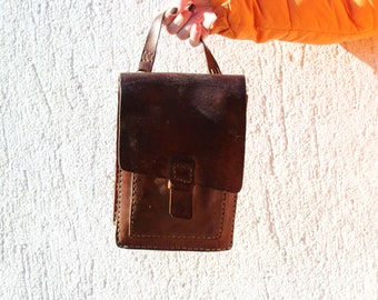 May include: A brown leather satchel bag with a flap closure and a stitched design. The bag has a top handle and a shoulder strap.