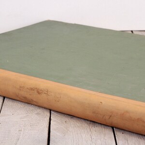 May include: A green, hardback book with a brown spine. The book is lying on a white wooden surface.
