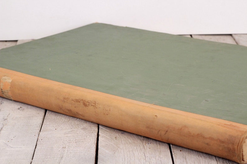 May include: A green, hardback book with a brown spine. The book is lying on a white wooden surface.