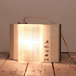 Può includere: Un apparecchio di illuminazione a parete bianco con un paralume in plastica trasparente e un cavo. La luce è accesa e il paralume è illuminato. L'apparecchio ha una serie di pulsanti etichettati "H", "3", "E" e "1".
