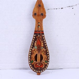 Peut inclure: Un petit instrument de musique en bois avec un corps en forme de poire et une tête pointue. Le corps est décoré de motifs floraux complexes en orange, vert et blanc. L'instrument a une corde qui descend au centre.