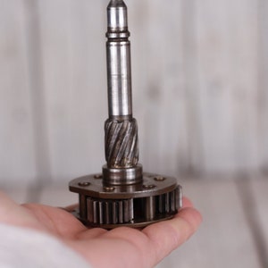 Peut inclure: Gros plan sur un engrenage métallique avec un long axe fin. L'engrenage a une série de dents autour de sa circonférence et est tenu dans une main.