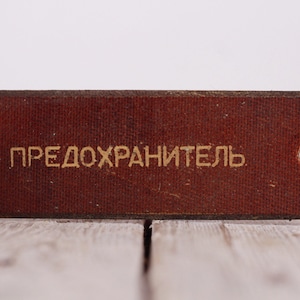 May include: A brown rectangular tag with two holes and the text "ПРЕДОХРАНИТЕЛЬ" in gold lettering.