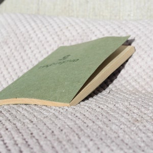 May include: A green, closed, hardcover journal with the word "repurpose" printed on the front cover. The journal is lying on a white, textured surface.