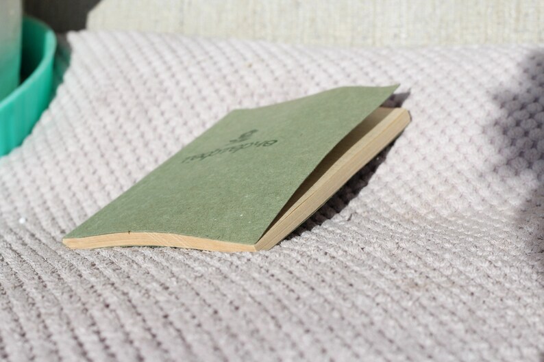May include: A green, closed, hardcover journal with the word "repurpose" printed on the front cover. The journal is lying on a white, textured surface.