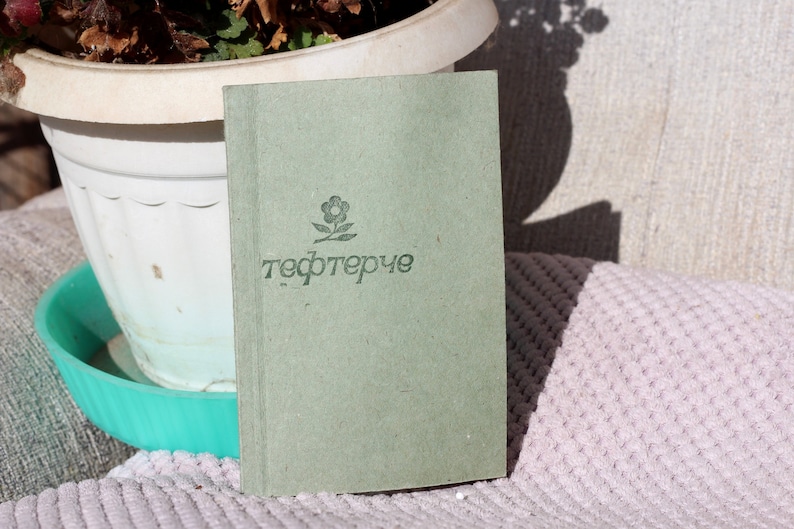 May include: A green notebook with a small flower design and the word "тефтерче" printed on the cover.