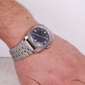 Könnte beinhalten: Eine silberne Armbanduhr mit blauem Zifferblatt und silbernen Zeigern. Die Uhr hat ein silbernes Metallband.