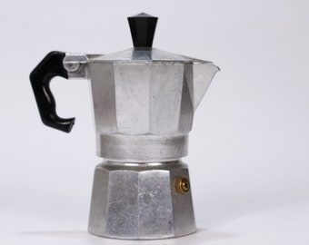 May include: A silver aluminum stovetop espresso maker with a black plastic handle and a black plastic lid.
